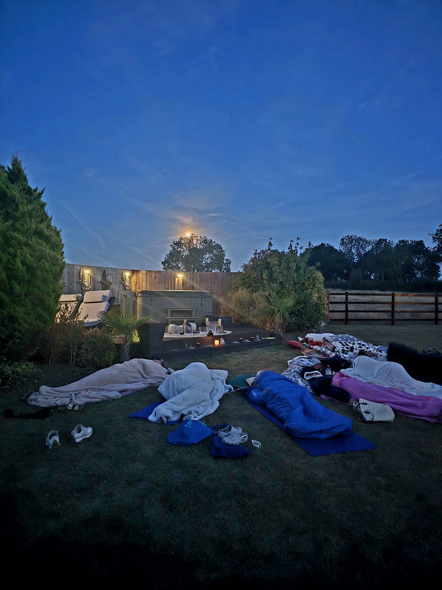 Guests wrapped in blankets on the grass under a full moon, ready for a sound bath
